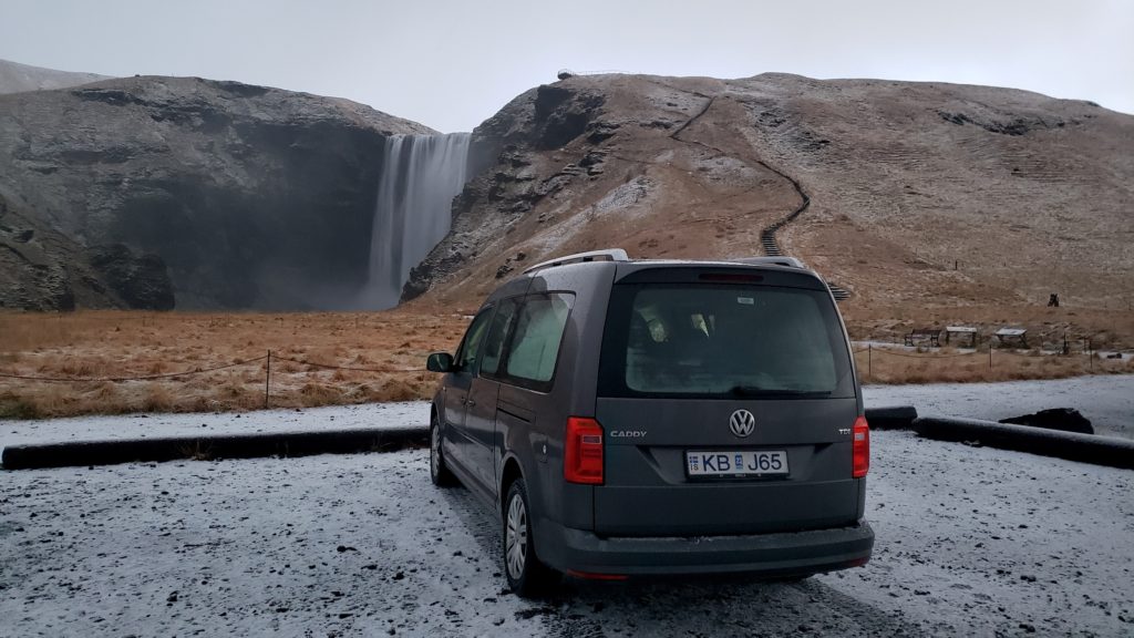 Van parked in front of snowy waterfall in winter in Iceland